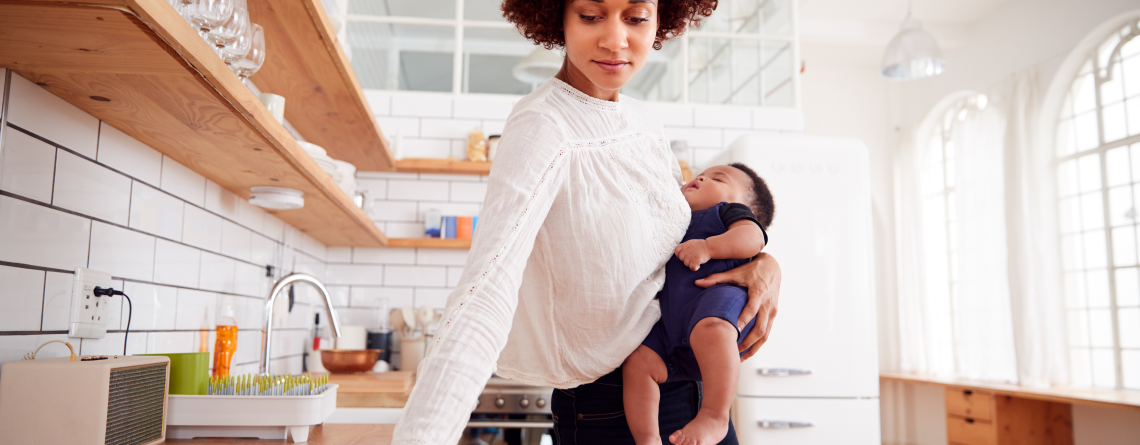 A busy woman holding a baby wipes down a kitchen counter