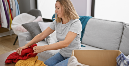 A blonde woman sitting on a couch, decluttering her apartment by putting clothes into storage