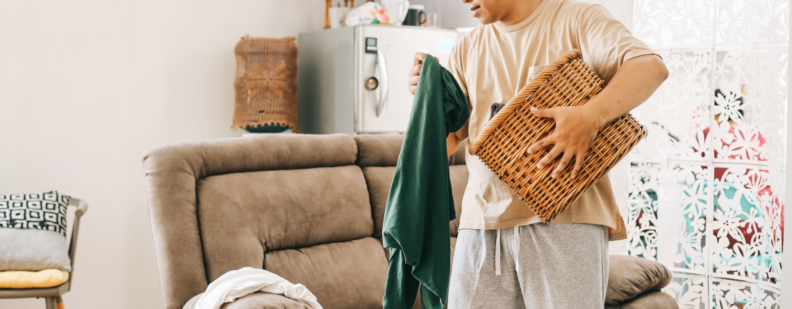 man picking up old clothes to put in a basket when cleaning his living room