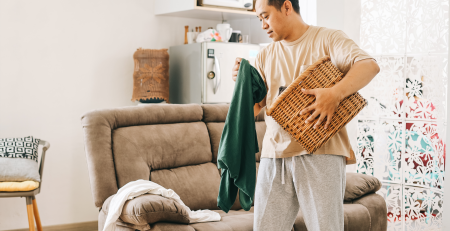 man picking up old clothes to put in a basket when cleaning his living room