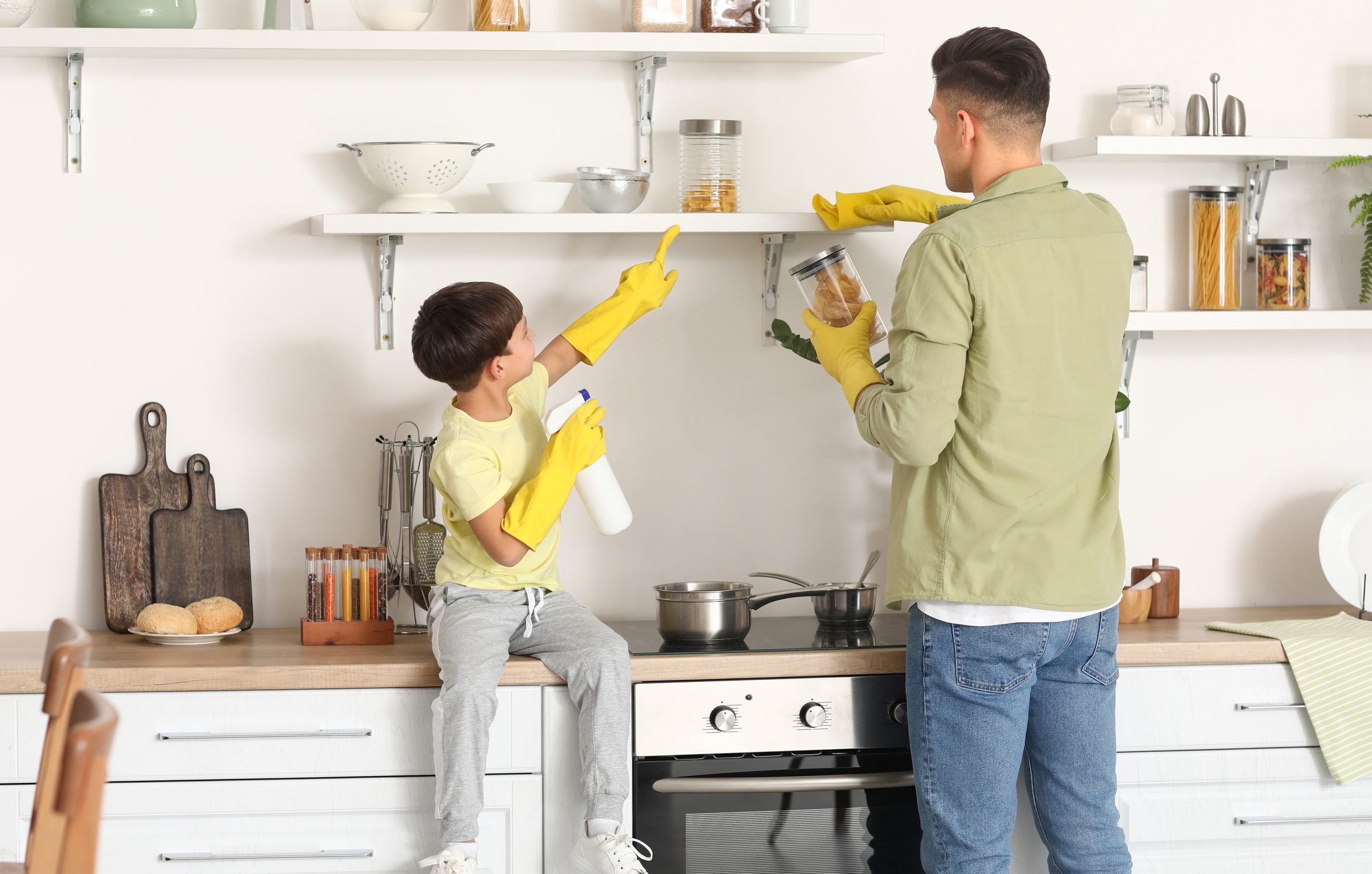 a father and young son wearing rubber gloves and cleaning their kitchen